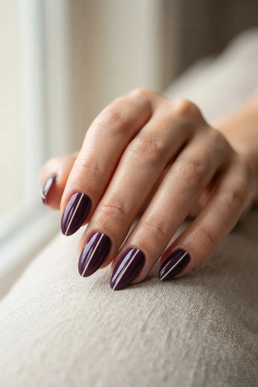 Deep plum almond nails with a fine cream stripe running lengthways