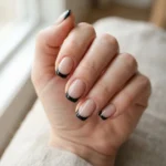 Sheer nude nails with a crisp black French tip on a short almond shape