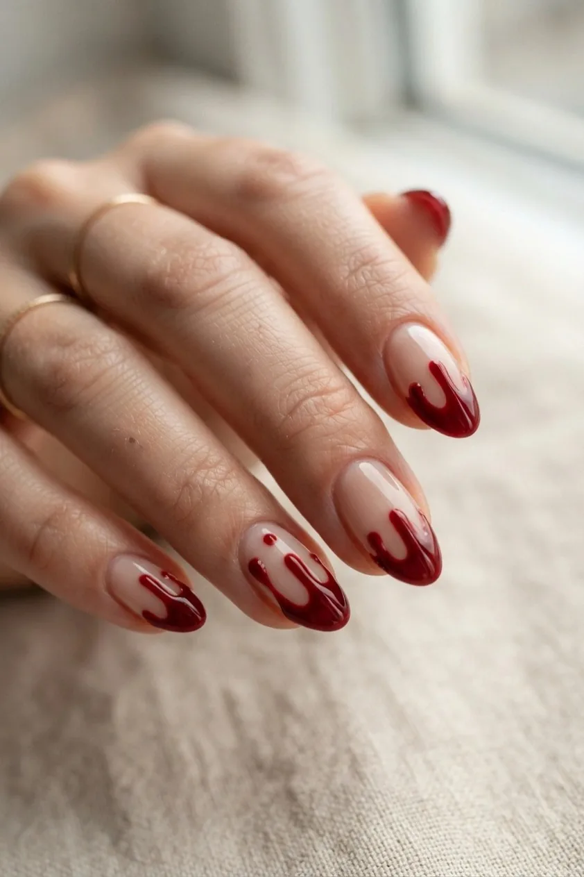 Nude nails with glossy red paint dripping down from the tip like blood