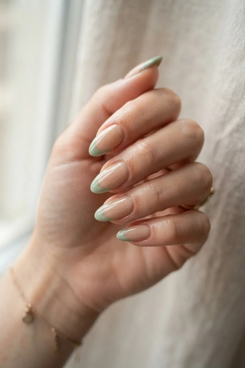 Almond nails with a soft sage green French tip over a warm nude base