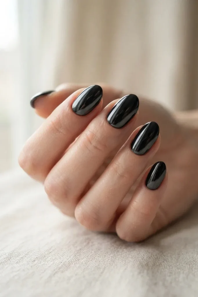 Short almond nails in a deep black mirror chrome finish reflecting the light