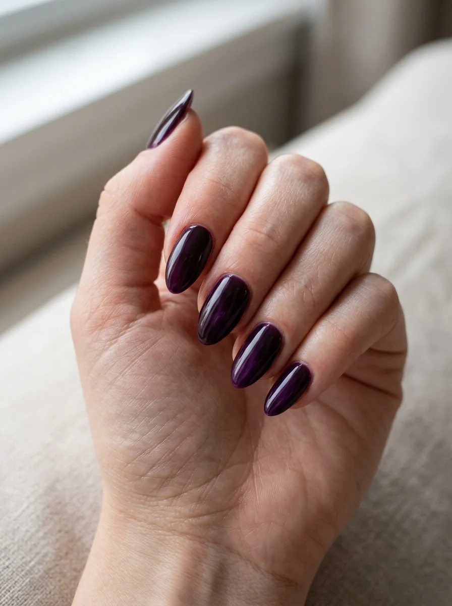 Photorealistic close-up of a hand with a full set of nails in a very dark plum showing purple depth in the light