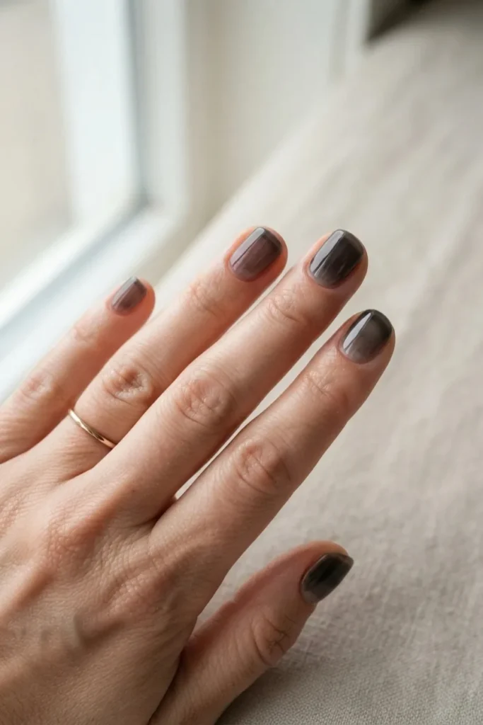Short nails in a sheer smoky black wash with the natural nail showing faintly through