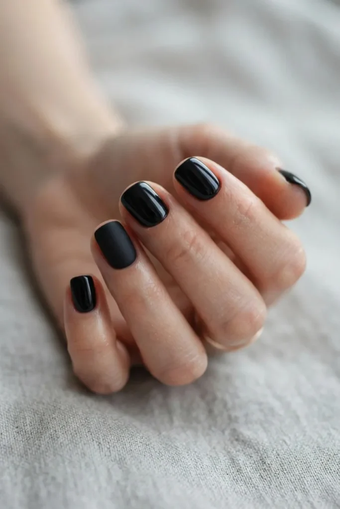 Short black nails with one matte accent nail among glossy black nails