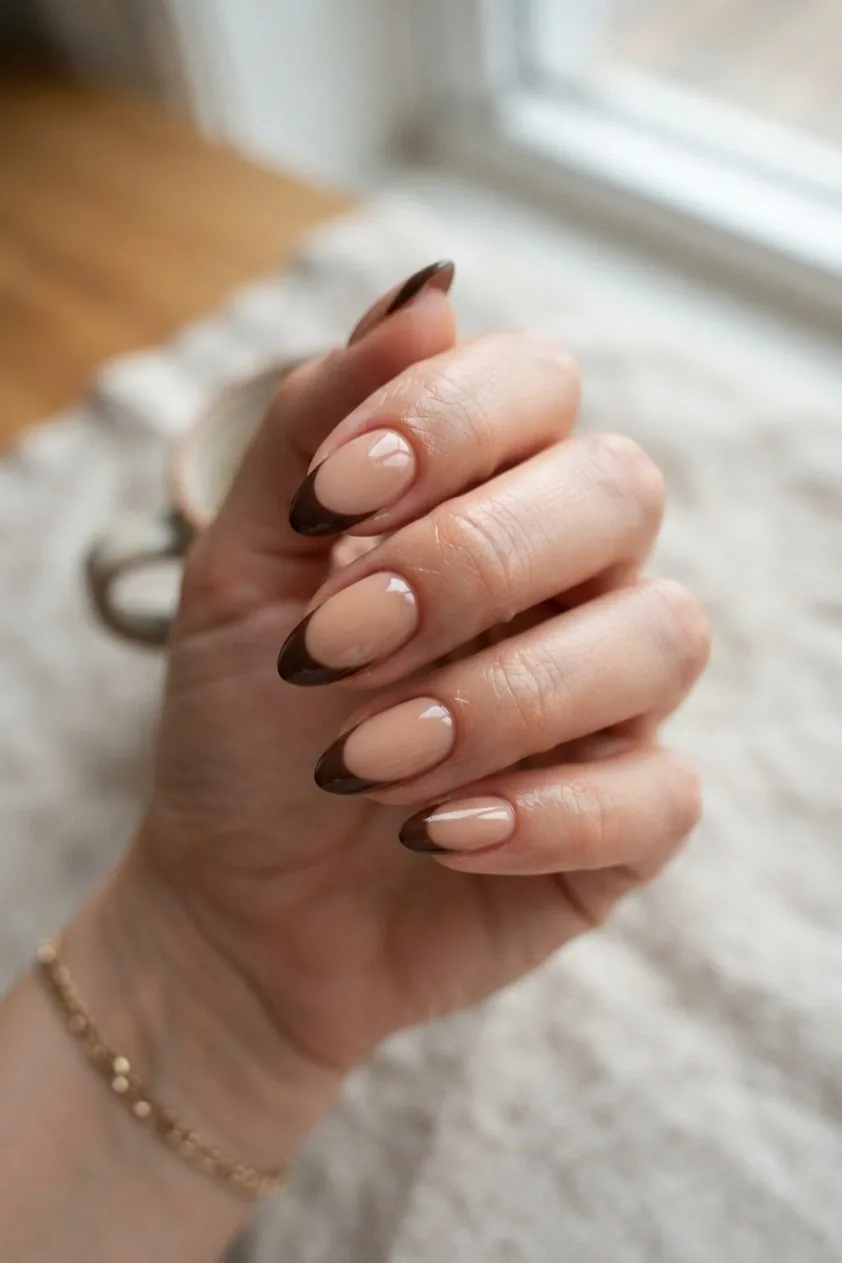 Almond nails with a chocolate brown French tip over a warm nude base