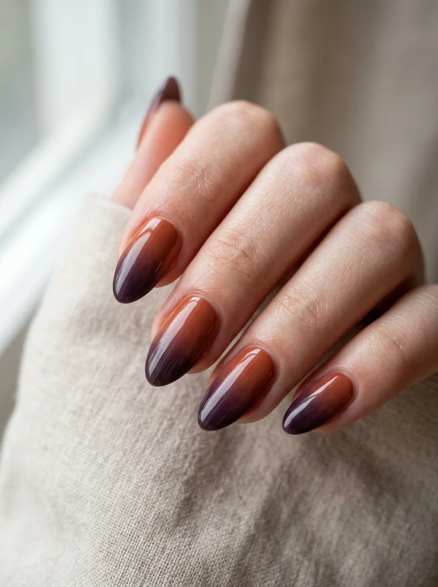 Photorealistic close-up of a hand with nails with a smooth gradient from warm rust at the cuticle to deep plum at the tips