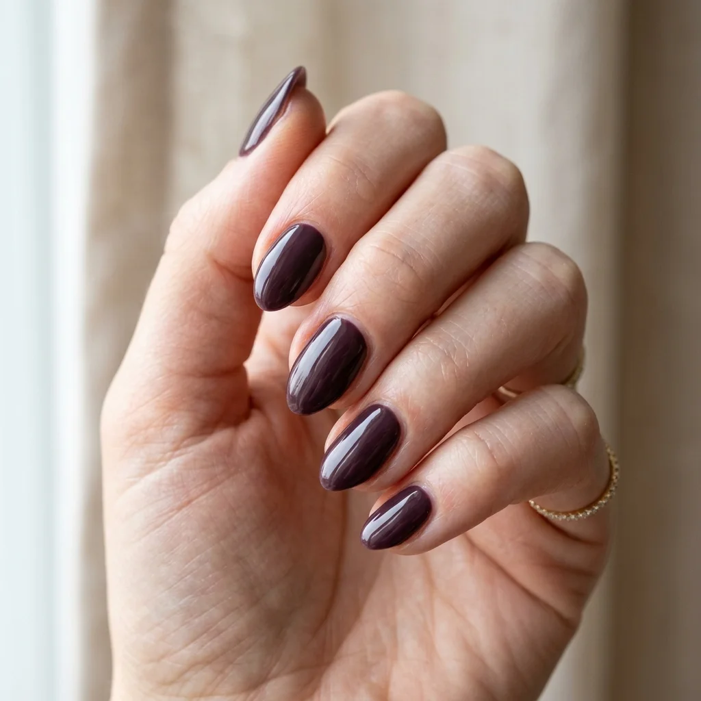 Photorealistic close-up of a hand with short almond nails in a glossy deep aubergine purple brown